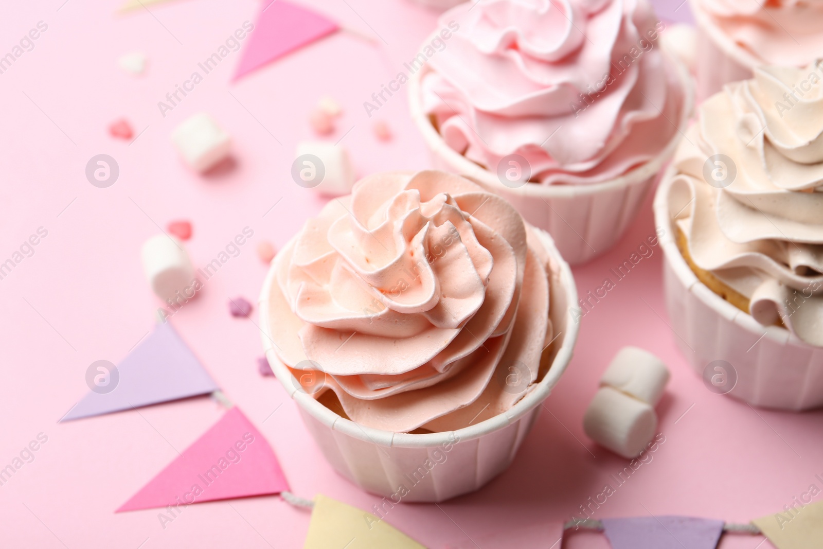 Photo of Delicious birthday cupcakes, bunting flags, marshmallows and sprinkles on pink background, closeup