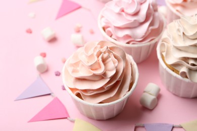 Photo of Delicious birthday cupcakes, bunting flags, marshmallows and sprinkles on pink background, closeup