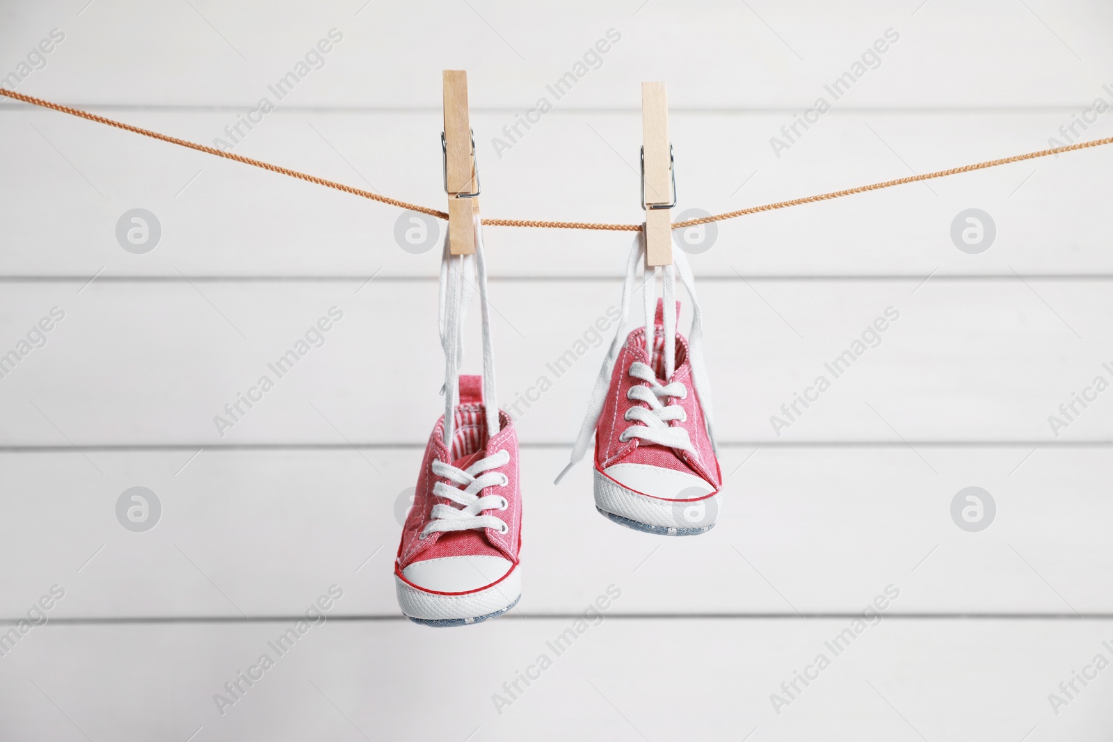 Photo of Cute pink baby sneakers drying on washing line against white wall