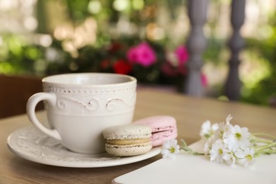 Photo of Cup of drink, macarons and flowers on table outdoors in morning