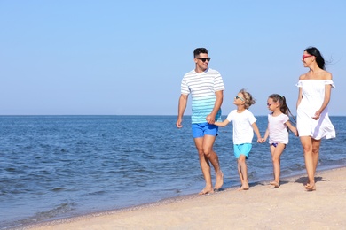 Photo of Happy family walking on sandy beach near sea, space for text. Summer holidays