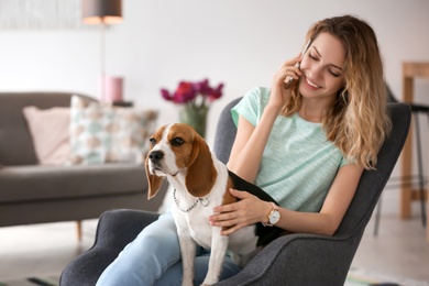 Photo of Young woman talking on phone while stroking her dog at home