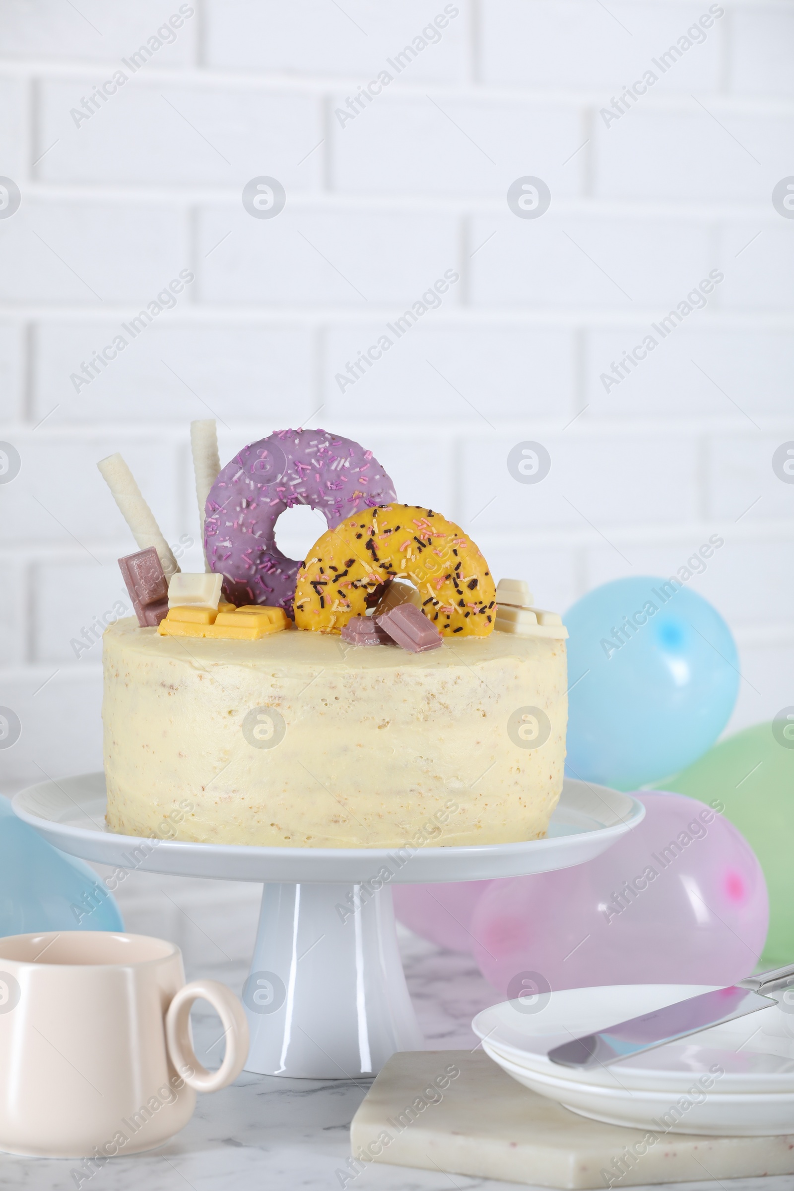 Photo of Delicious cake decorated with sweets, tableware and balloons on white marble table, space for text