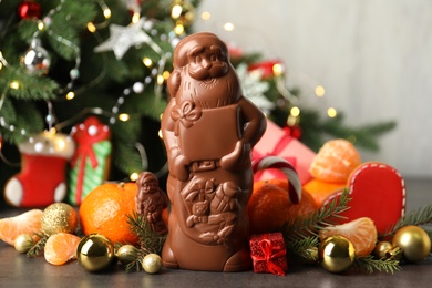 Photo of Composition with chocolate Santa Claus candies on grey table near Christmas tree, closeup