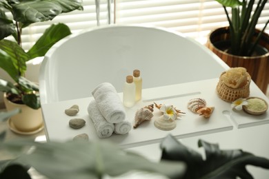 Photo of Bath tray with spa products, towels and shells on tub in bathroom