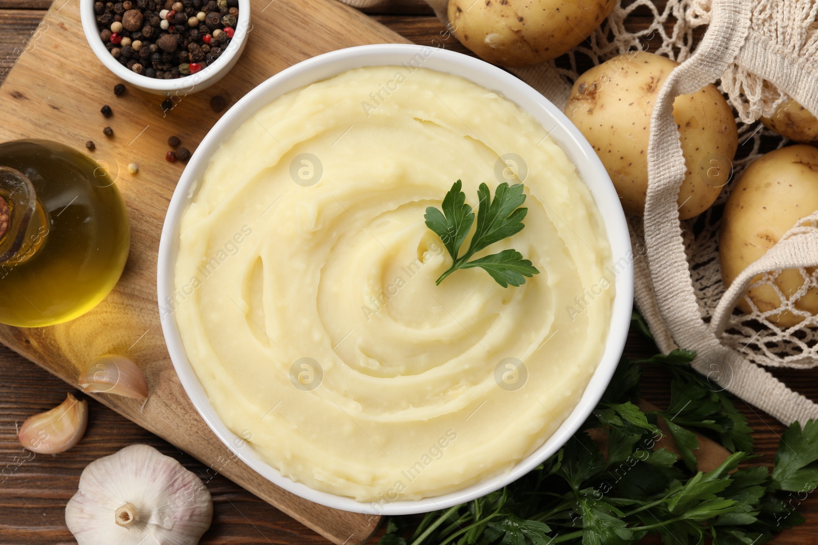 Photo of Bowl of tasty mashed potato, parsley, garlic, olive oil and pepper on wooden table, flat lay