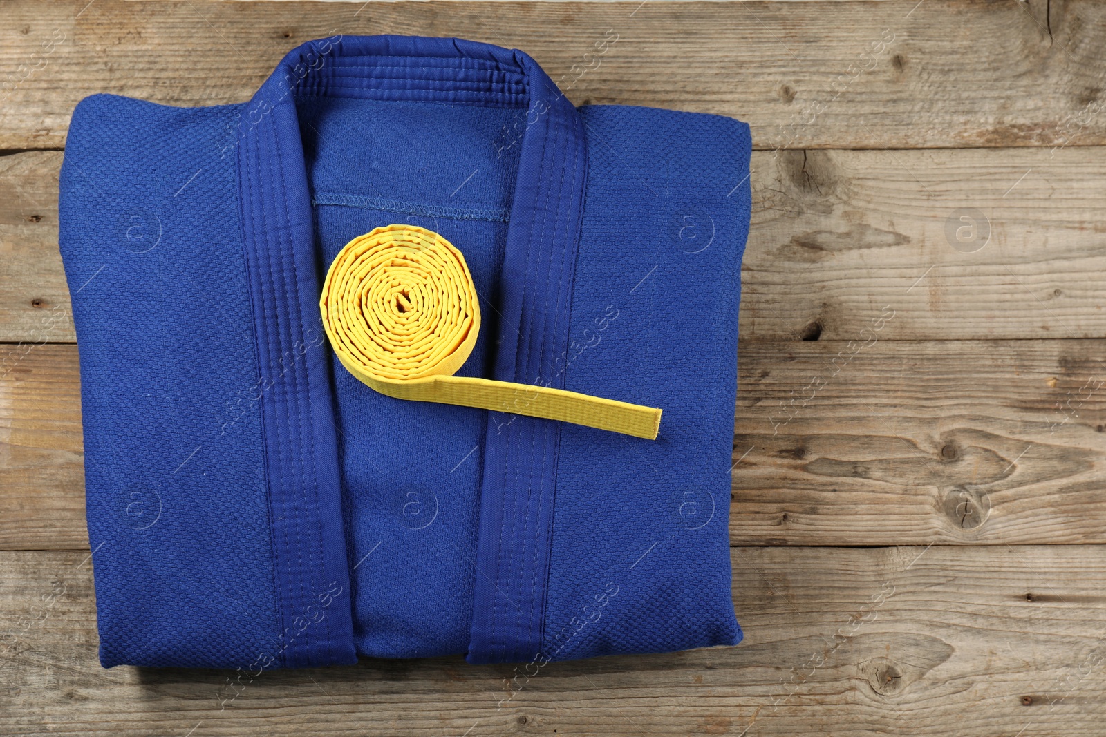 Photo of Yellow karate belt and blue kimono on wooden background, top view. Space for text