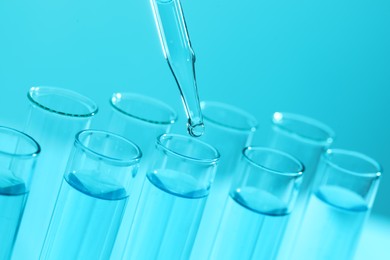 Dripping liquid from pipette into test tube on light blue background, closeup. Laboratory analysis