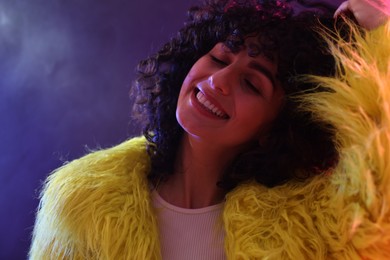 Beautiful young woman in yellow fur coat on color background in neon lights, closeup