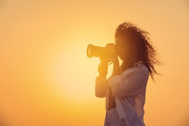 African American photographer taking photo with professional camera outdoors at sunset