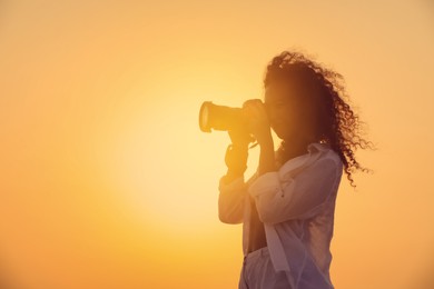 Photo of African American photographer taking photo with professional camera outdoors at sunset