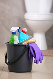 Photo of Bucket with cleaning supplies on floor in bathroom