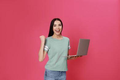 Emotional young woman with modern laptop on pink background