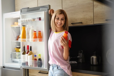 Woman with bottle of juice near refrigerator in kitchen