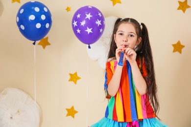 Adorable girl with party blower and decor for birthday celebration on color background