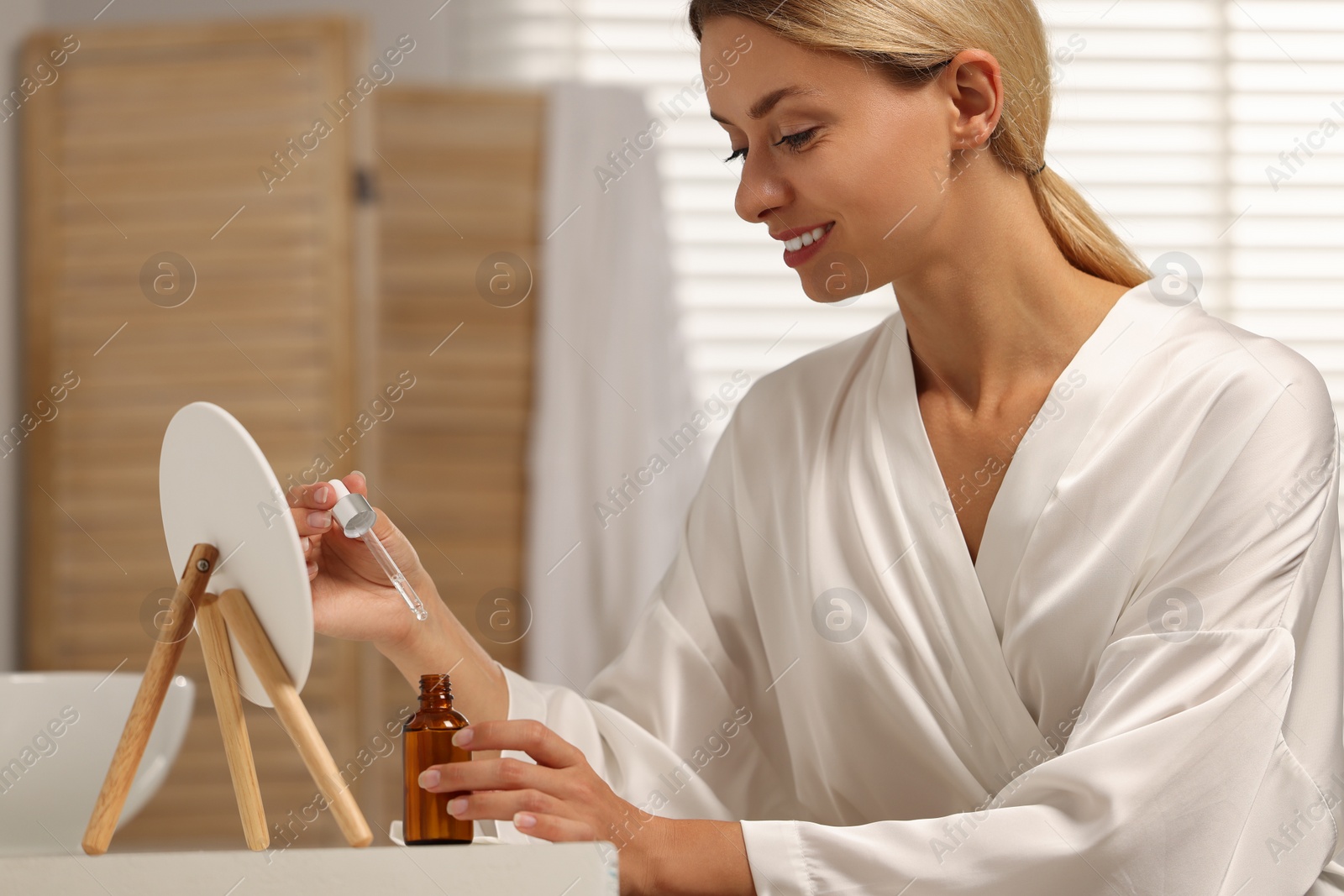 Photo of Beautiful woman with cosmetic serum at table in bathroom