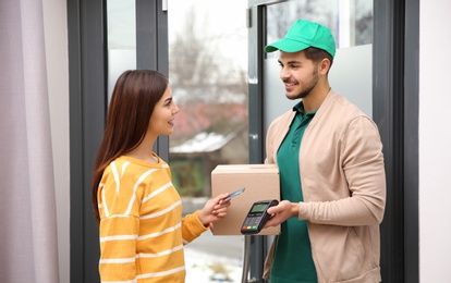 Young woman with credit card using bank terminal for delivery payment at doorway