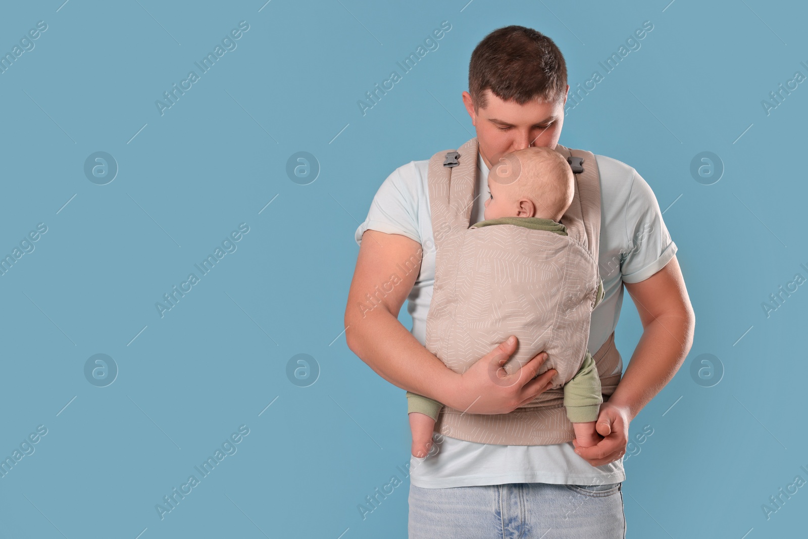 Photo of Father holding his child in sling (baby carrier) on light blue background. Space for text