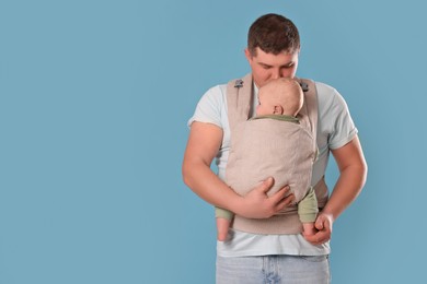 Father holding his child in sling (baby carrier) on light blue background. Space for text