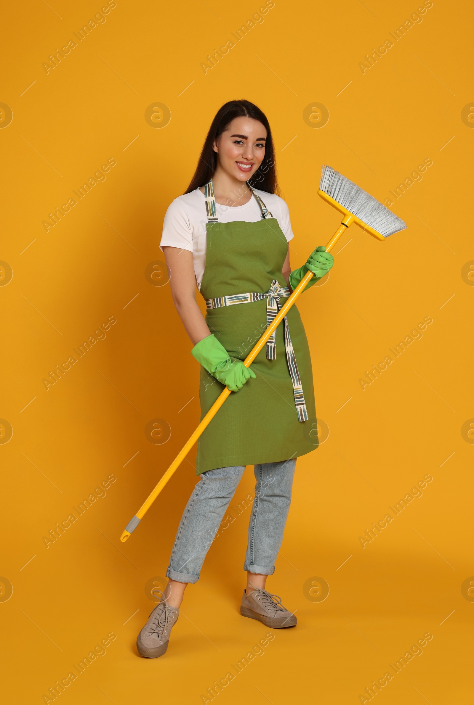 Photo of Beautiful young woman with broom on yellow background