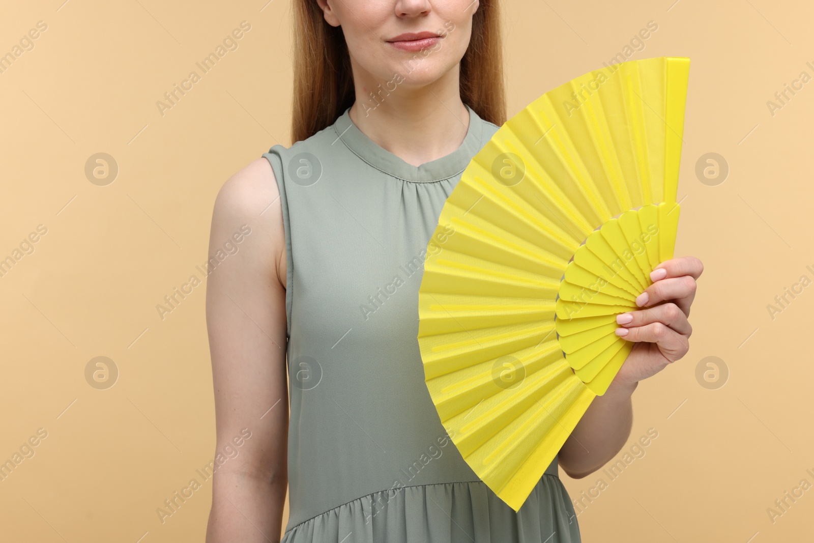 Photo of Woman with yellow hand fan on beige background, closeup