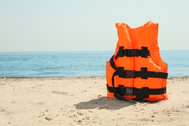 Photo of Orange life jacket on sandy beach near sea. Emergency rescue equipment