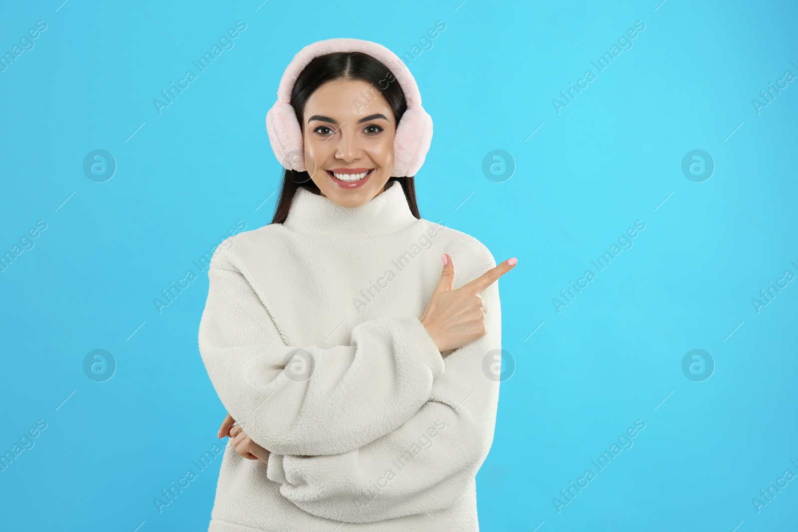 Photo of Beautiful young woman wearing earmuffs on light blue background. Space for text