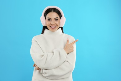 Photo of Beautiful young woman wearing earmuffs on light blue background. Space for text