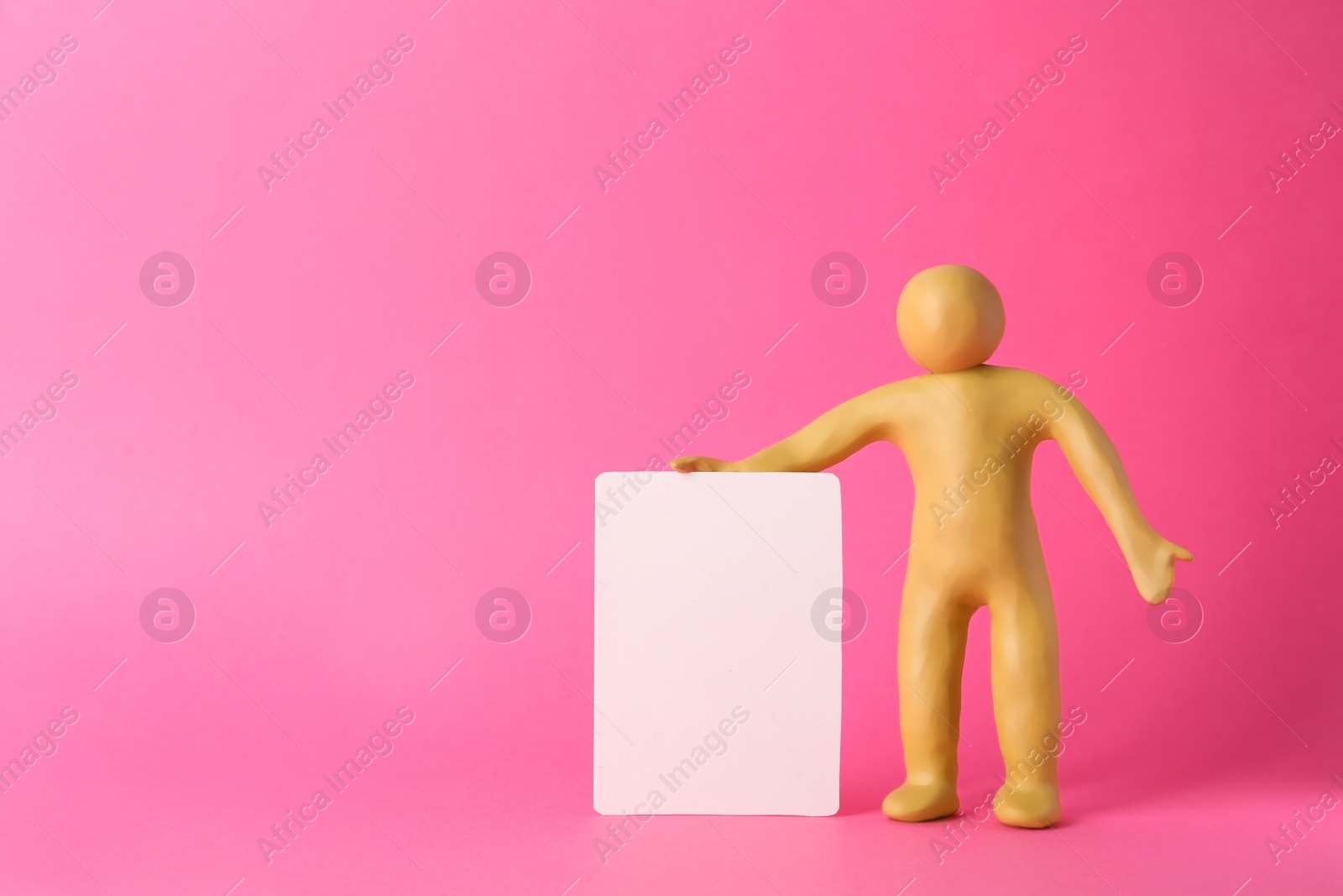 Photo of Human figure made of yellow plasticine holding blank sign on pink background. Space for text