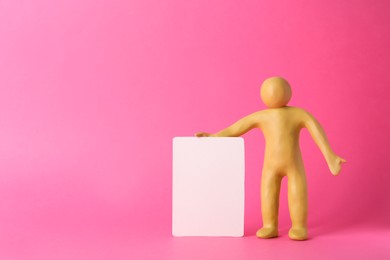 Photo of Human figure made of yellow plasticine holding blank sign on pink background. Space for text
