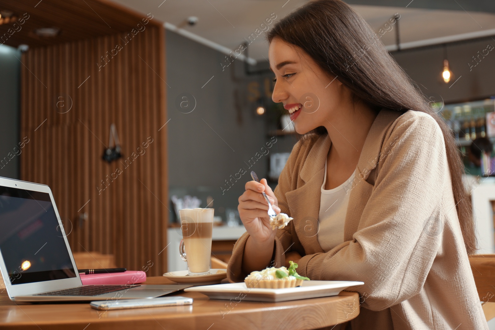 Photo of Young blogger with laptop eating cake in cafe