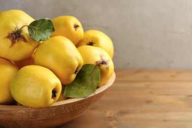 Photo of Tasty ripe quince fruits in bowl on wooden table, closeup. Space for text