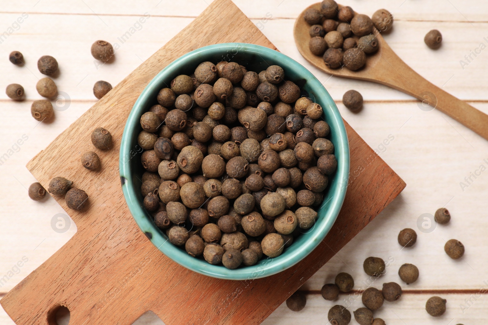 Photo of Dry allspice berries (Jamaica pepper) in bowl and spoon on light wooden table, flat lay