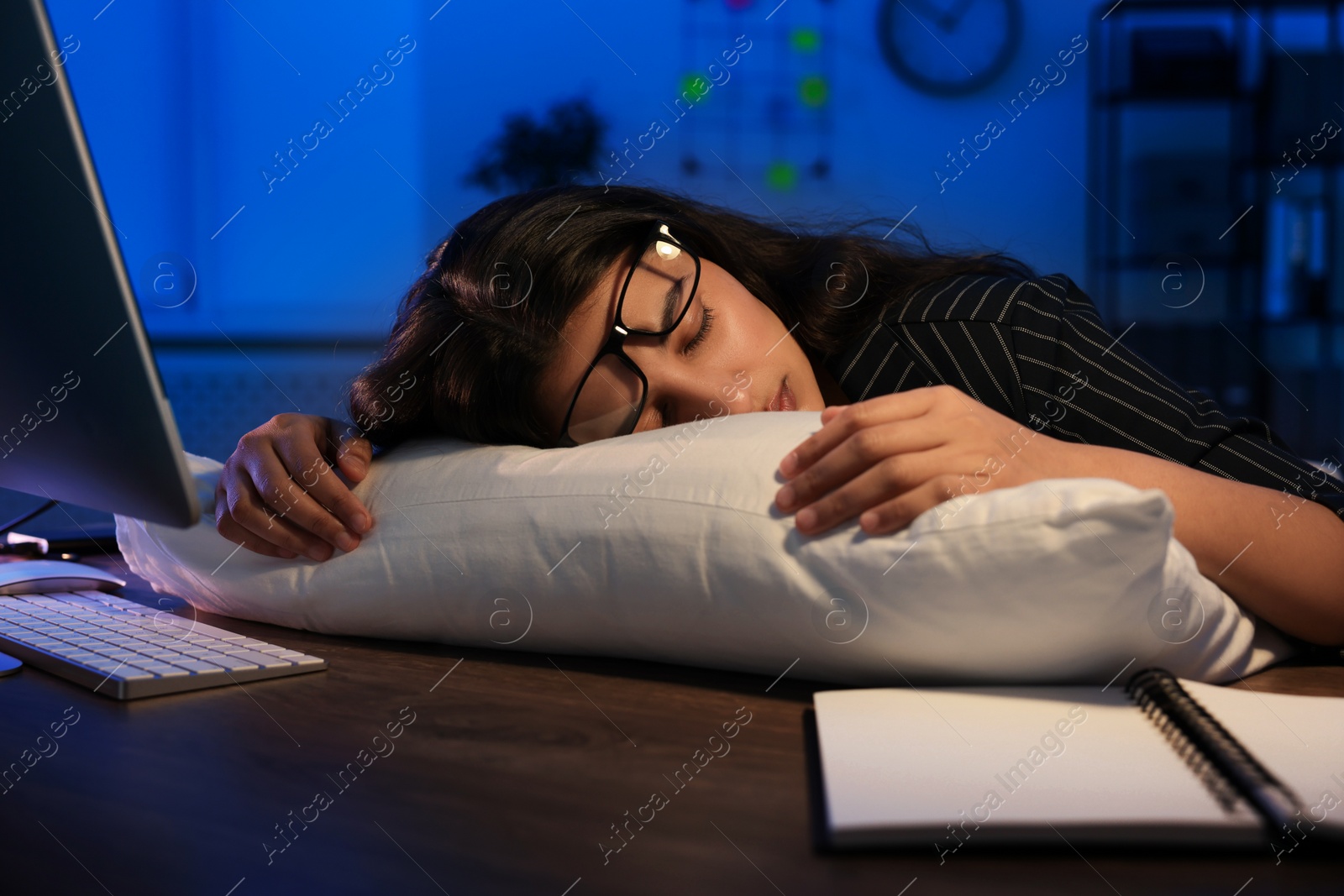 Photo of Tired overworked businesswoman napping with pillow at night in office