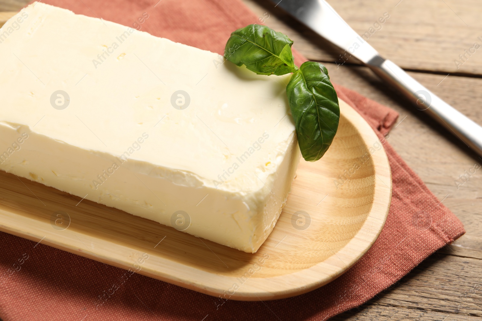 Photo of Block of tasty butter with basil and knife on wooden table, closeup