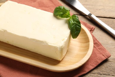 Block of tasty butter with basil and knife on wooden table, closeup