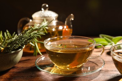 Photo of Cup of aromatic herbal tea, fresh rosemary and thyme on wooden table