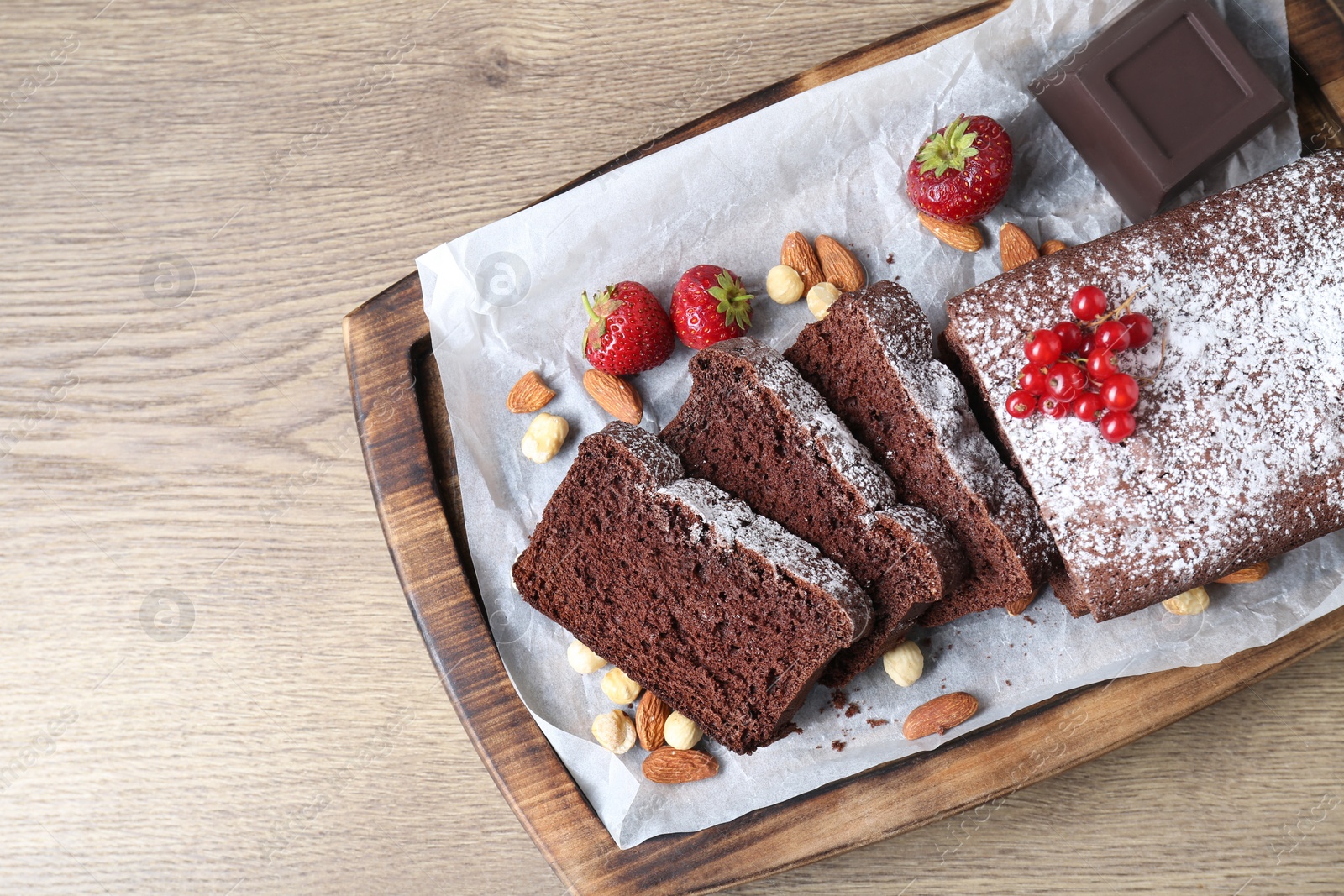 Photo of Tasty chocolate sponge cake with berries and nuts on wooden table, top view. Space for text