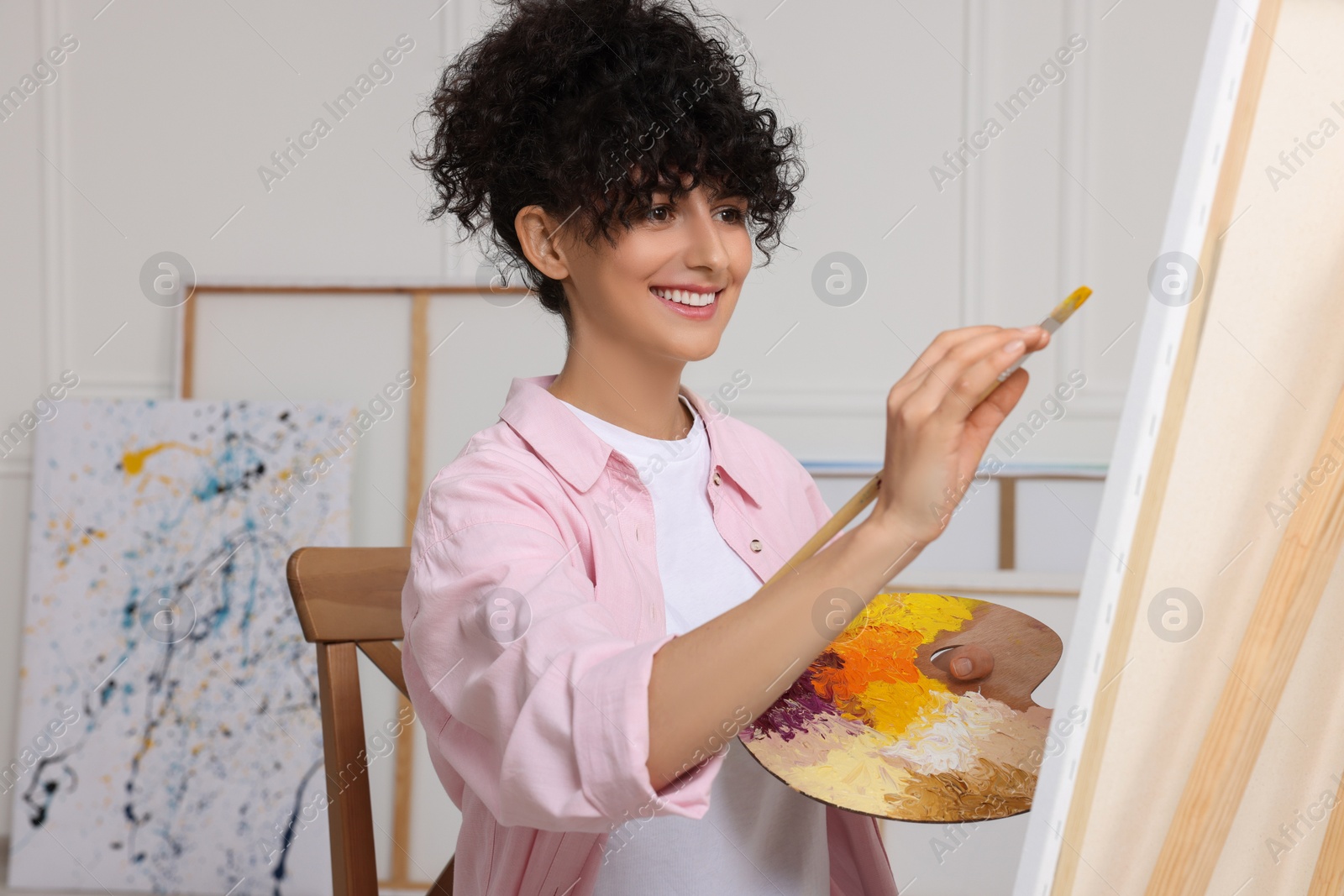 Photo of Young woman painting on easel with canvas in studio