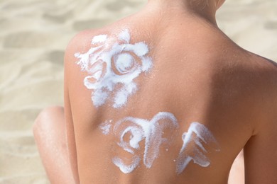 Child with abbreviation SPF 50 of sunscreen on back at beach, closeup