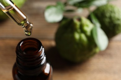 Dripping bergamot essential oil into glass bottle on table, closeup