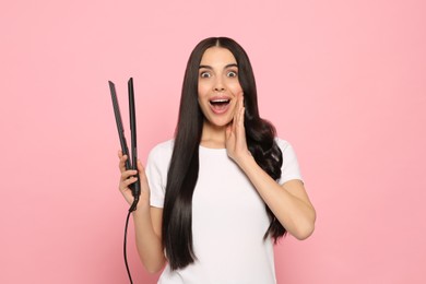 Beautiful emotional woman with hair iron on pink background