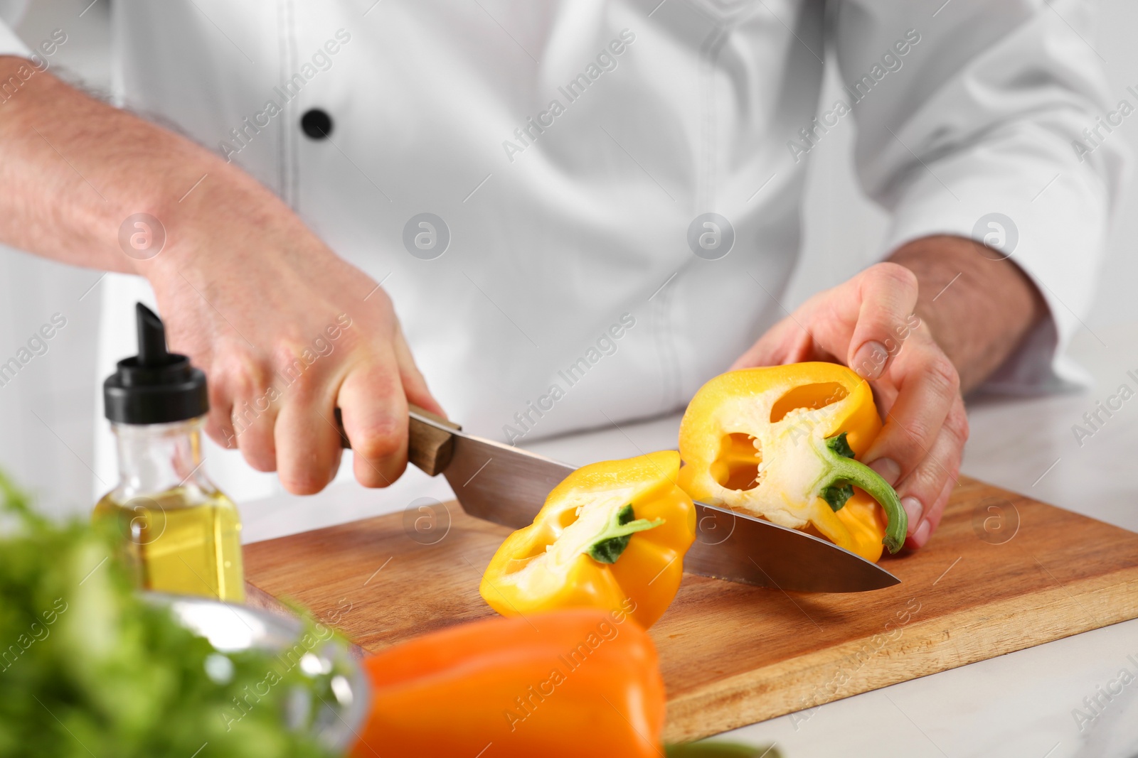 Photo of Chef cutting bell pepper at marble table in kitchen, closeup