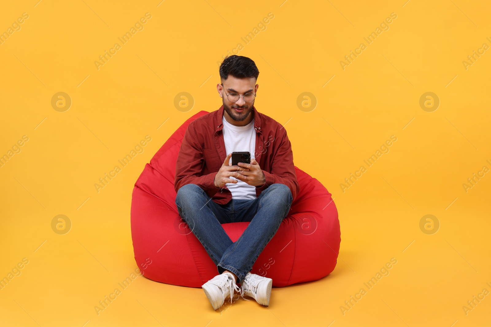 Photo of Handsome young man using smartphone on bean bag chair against yellow background