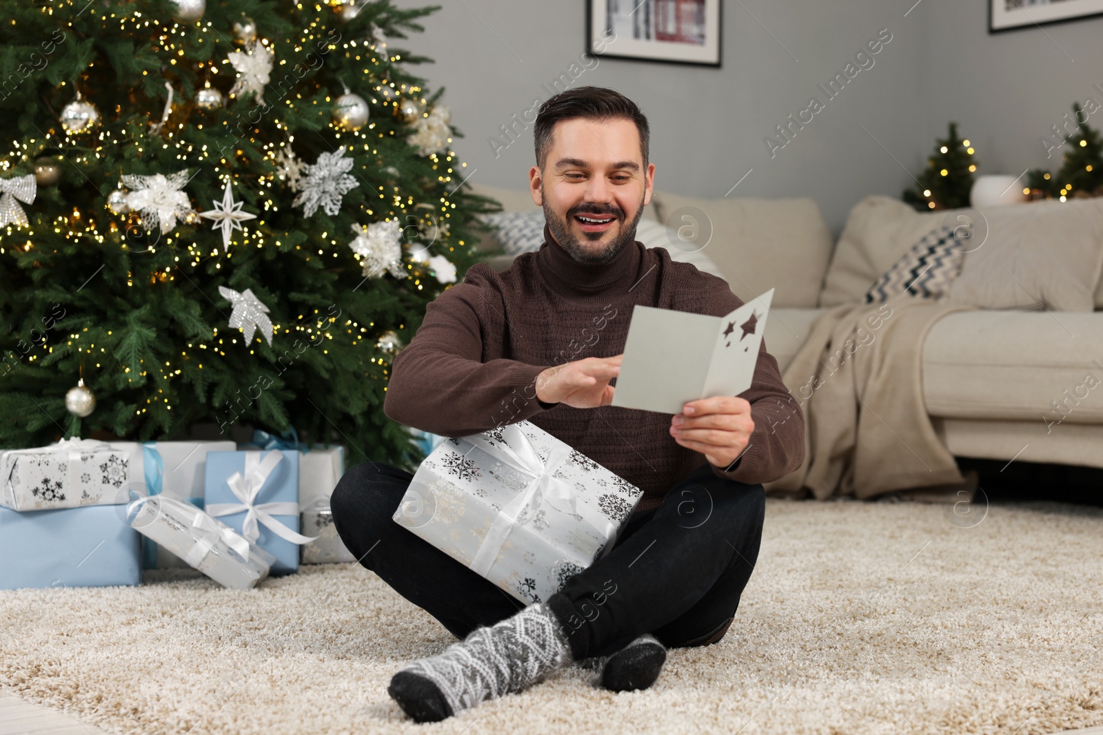 Photo of Happy man with Christmas gift reading greeting card at home
