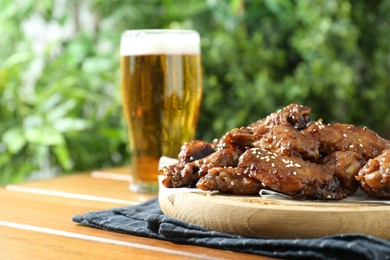Photo of Tasty roasted chicken wings and glass of beer on wooden table, closeup. Space for text