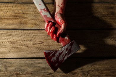 Photo of Man holding bloody axe on wooden surface, top view