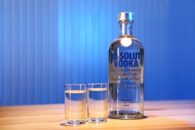 MYKOLAIV, UKRAINE - SEPTEMBER 23, 2019: Absolut vodka and shot glasses on wooden bar counter. Space for text