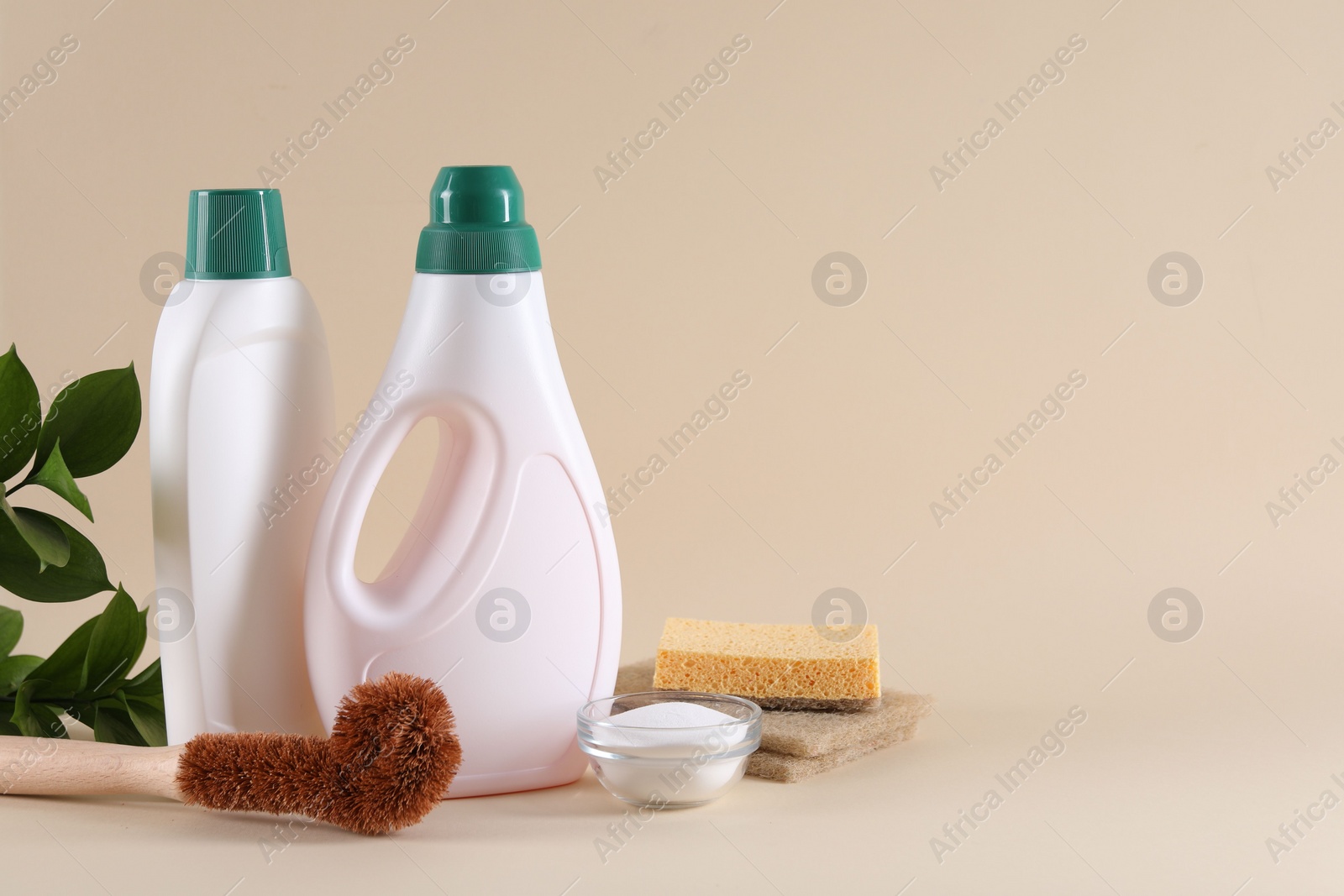 Photo of Bottles of cleaning product, sponges, brush and baking soda on beige background. Space for text