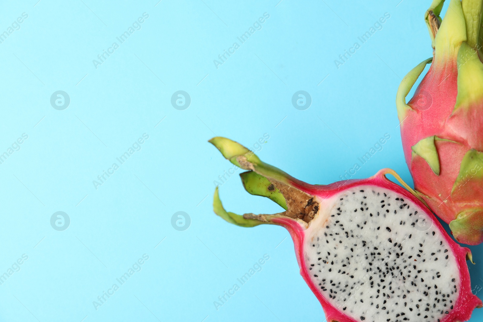 Photo of Delicious cut and whole dragon fruits (pitahaya) on light blue background, flat lay. Space for text